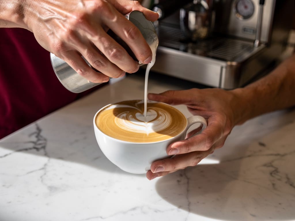 Barista che prepara un cappuccino con latte art su un bancone in marmo